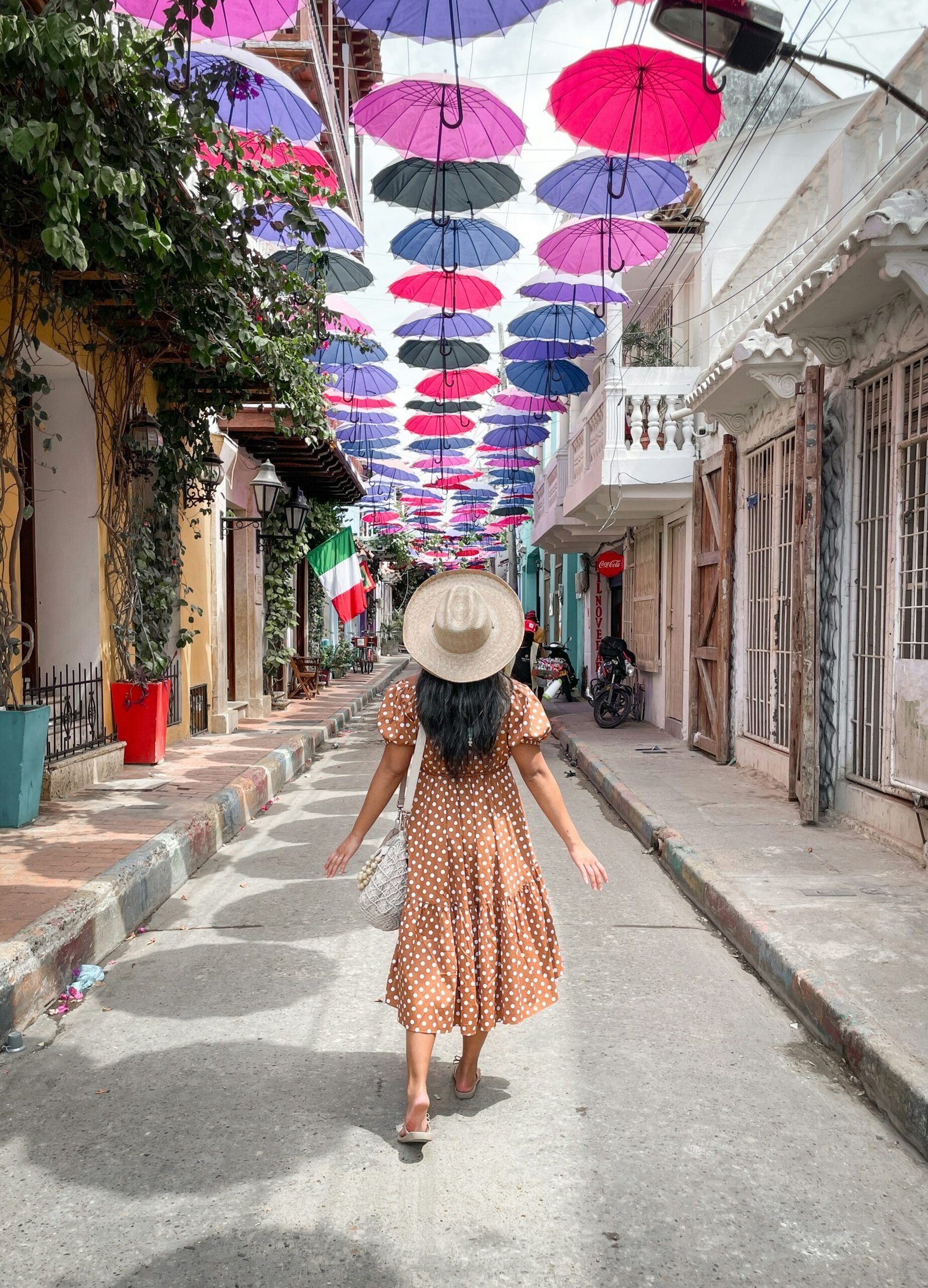 a woman in a dress and hat walking down a street