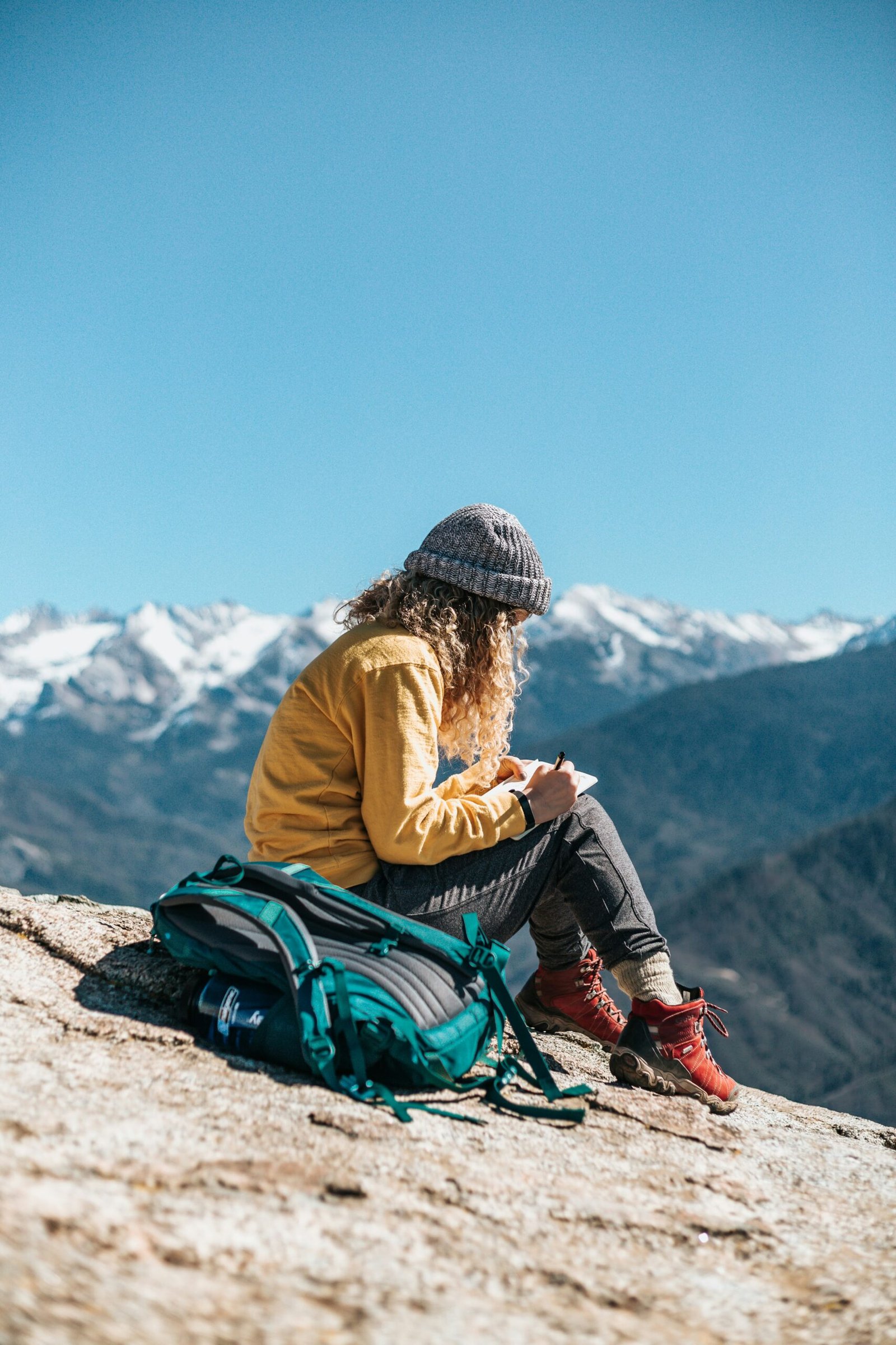 woman writing while sitting on hill near mountain