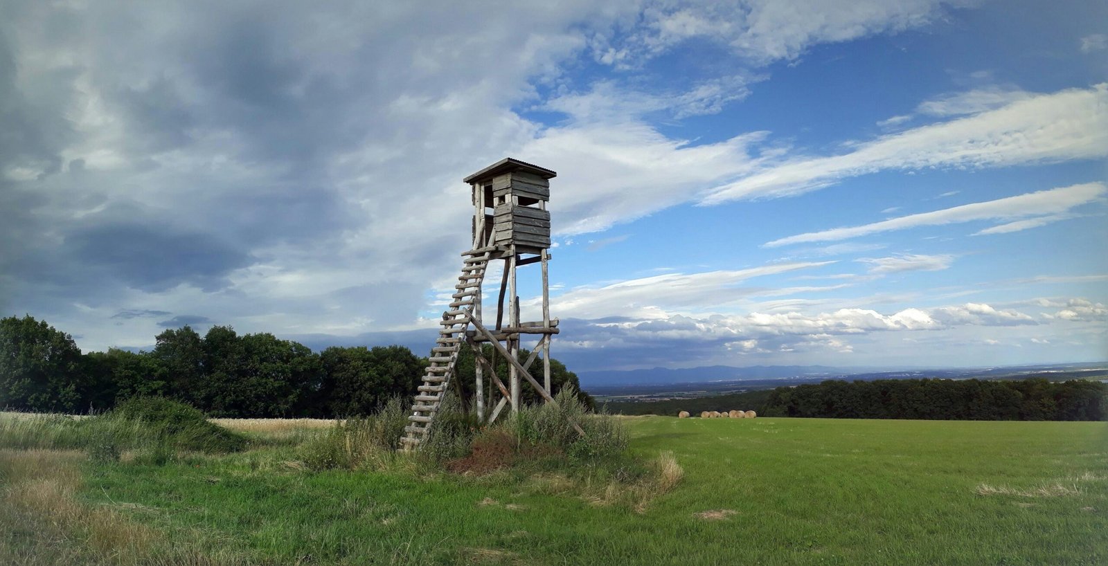 brown wooden tower on green grass field under blue sky and white clouds during daytime